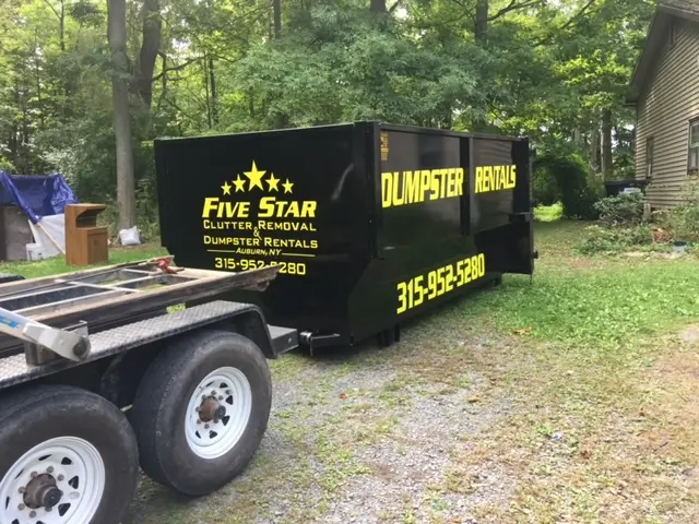 A truck with a black dumpster parked in front of a house.